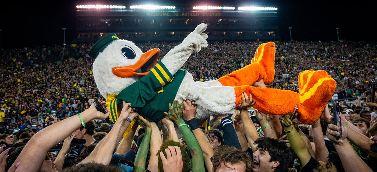 UO Duck mascot being passed overhead by a large group of football fans