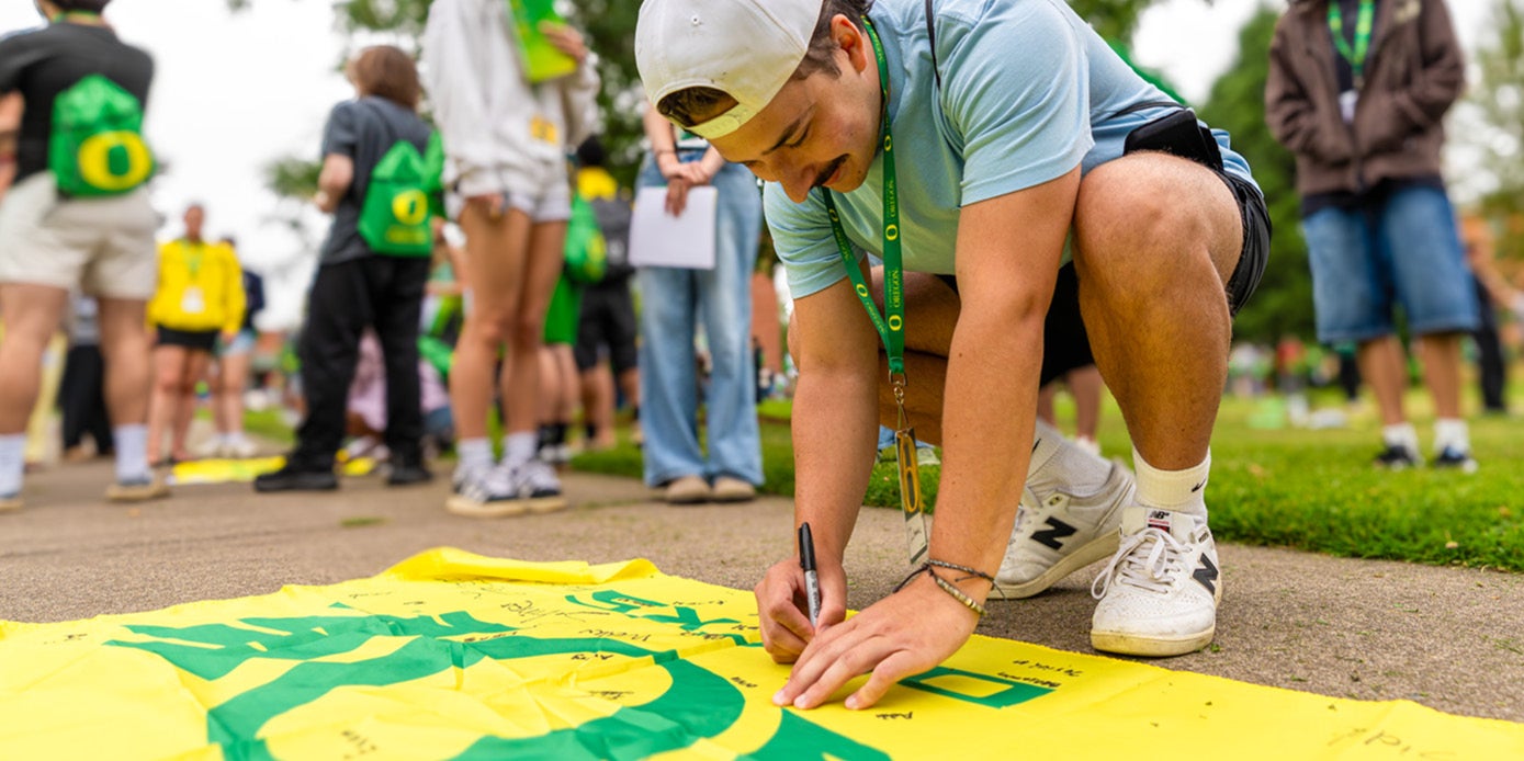 A student crouching over a UO Ducks flag, signing their name