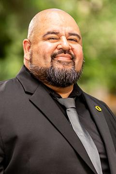 Profile photo of Luis Renteria wearing a black suit, grey tie, and green UO logo lapel pin