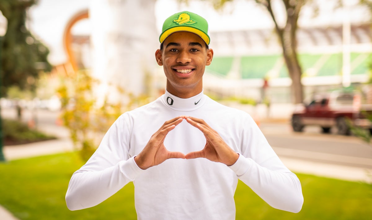 Anthony Trucks making his hands into an Oregon "O" wearing a green logo baseball cap